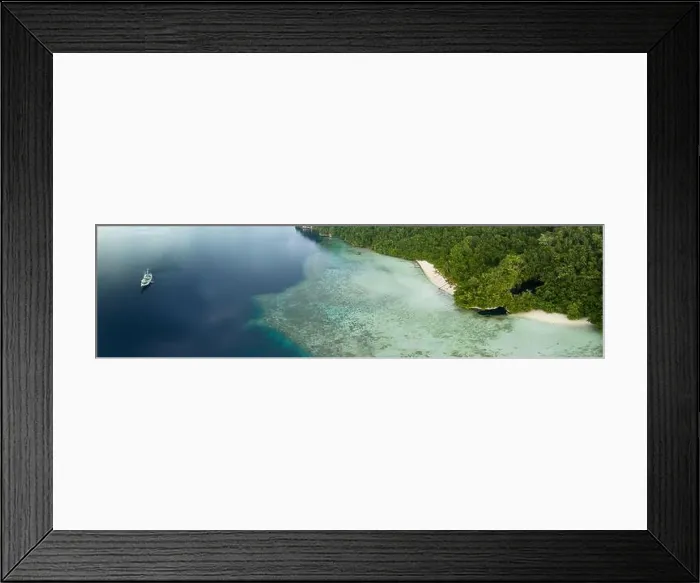 Framed Print : The mouth of a dark, water-filled cave opens on the edge of a forest-covered limestone island near Fak Fak, Indonesia. Limestone often harbors caves