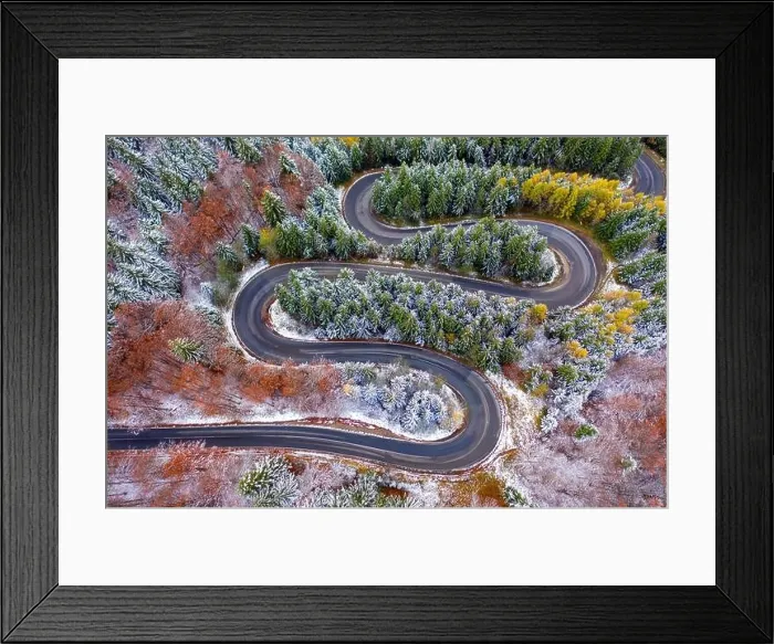 Framed Print : Aerial view of a winding mountain road passing through a fir trees forest. Winter with snow