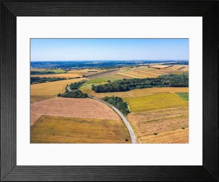 Framed Print : Aerial view of a country road amid fields against blue clear sky Framed Print : Aerial view of a country road amid fields against blue clear sky