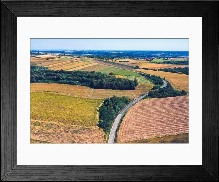 Framed Print : Aerial view of a country road amid fields against blue clear sky Framed Print : Aerial view of a country road amid fields against blue clear sky