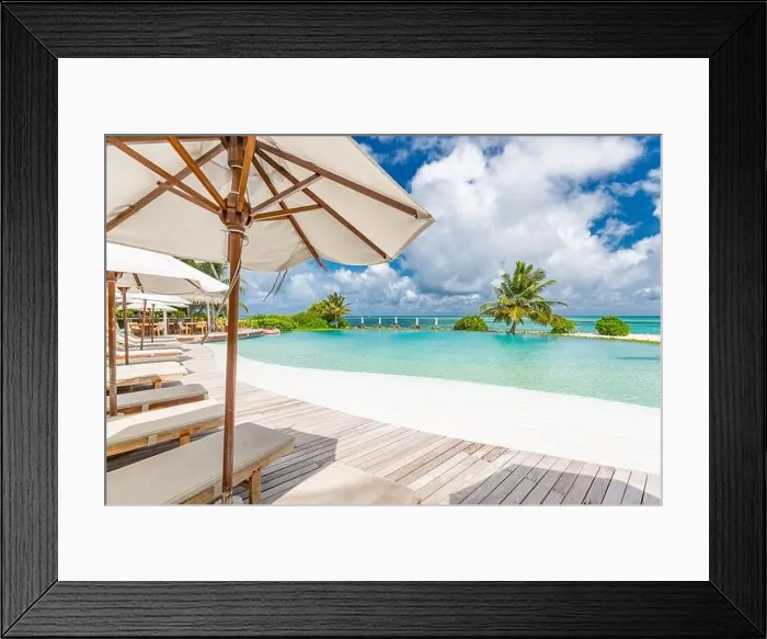 Framed Print : Summer outdoor tourism landscape. Luxurious beach resort with swimming pool and beach chairs or loungers under umbrellas with palm trees and blue sky Framed Print : Summer outdoor tourism landscape. Luxurious beach resort with swimming pool and beach chairs or loungers under umbrellas with palm trees and blue sky