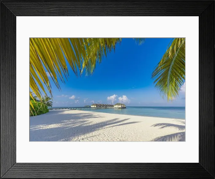 Framed Print : Luxury hotel with water villas and palm tree leaves over white sand close to blue sea seascape. Tranquil paradise landscape, seaside sunny destination
