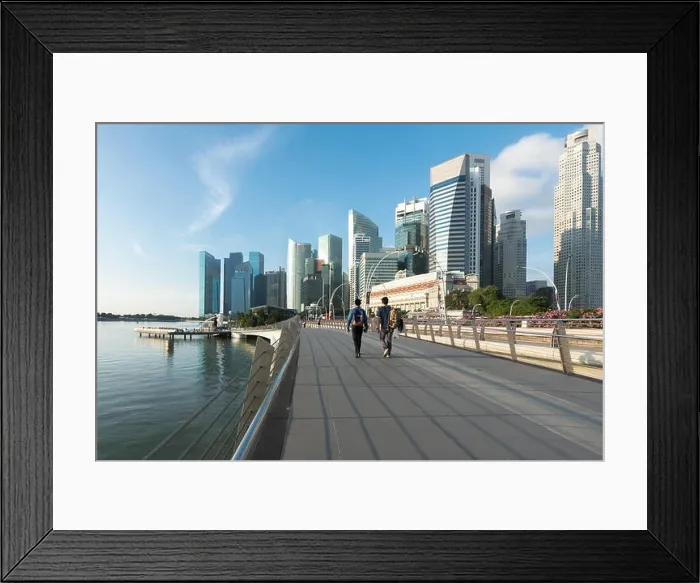 Framed Print : Pedestrians walk along bridge near Marina bay in Singapore with Singapore skyscraper and Merlion park in background Framed Print : Pedestrians walk along bridge near Marina bay in Singapore with Singapore skyscraper and Merlion park in background