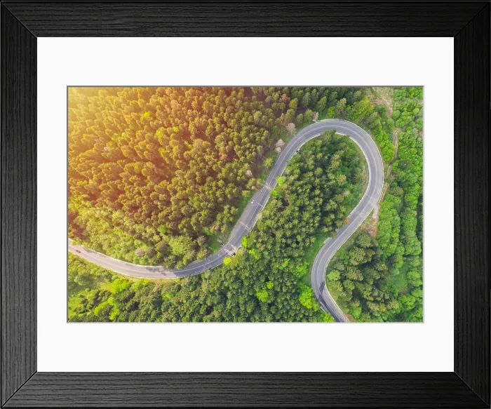 Framed Print : Aerial view of a forest road passing through a fir trees forest