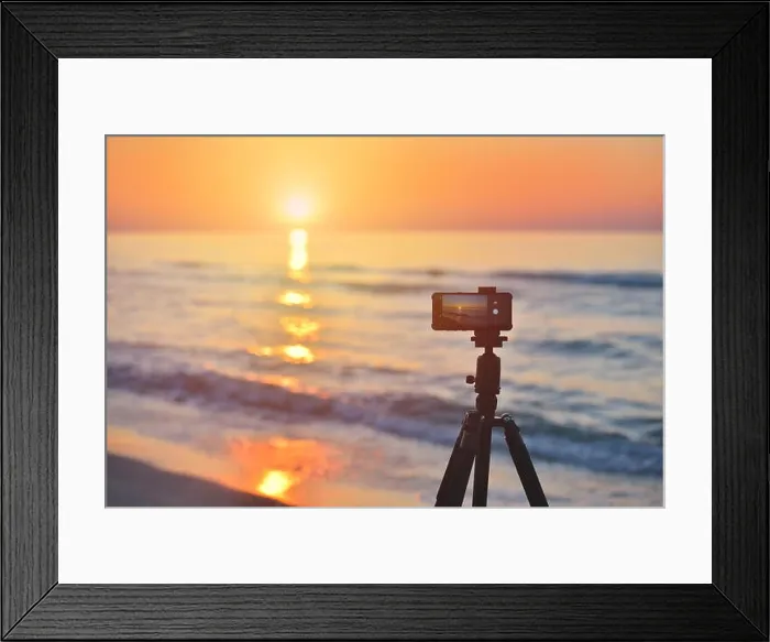Framed Print : Sunrise over the sea coast. Fireball of the sun above the horizon in a colorful orange sky. Smartphone camera on a tripod in the foreground Framed Print : Sunrise over the sea coast. Fireball of the sun above the horizon in a colorful orange sky. Smartphone camera on a tripod in the foreground