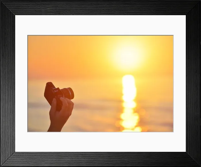 Framed Print : Sunrise over the sea coast. Fireball of the sun above the horizon in a colorful orange sky. Vintage SLR camera in hand in the foreground Framed Print : Sunrise over the sea coast. Fireball of the sun above the horizon in a colorful orange sky. Vintage SLR camera in hand in the foreground