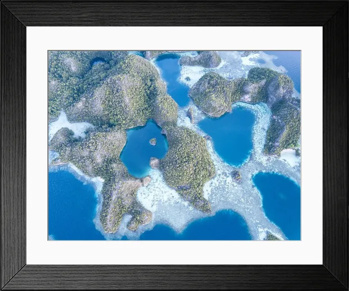 Framed Print : A bird's eye view shows dramatic limestone islands surrounding coral reefs in the peaceful, tropical seascape in Raja Ampat, Indonesia Framed Print : A bird's eye view shows dramatic limestone islands surrounding coral reefs in the peaceful, tropical seascape in Raja Ampat, Indonesia