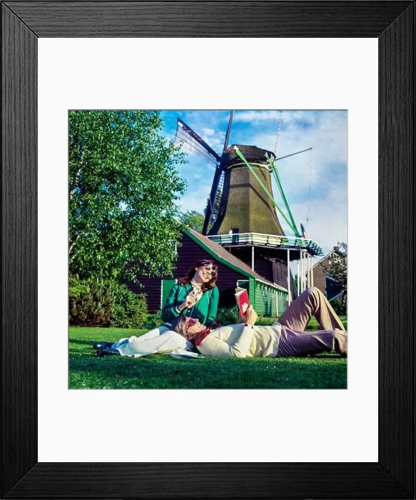 Framed Print : Vintage Netherlands 1970s, couple of middle aged tourists relaxing in meadow beside a windmill, Holland, Europe