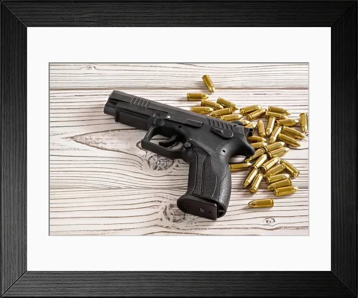 Framed Print : Black metal gun with brass ammo bullets on white wooden boards Framed Print : Black metal gun with brass ammo bullets on white wooden boards