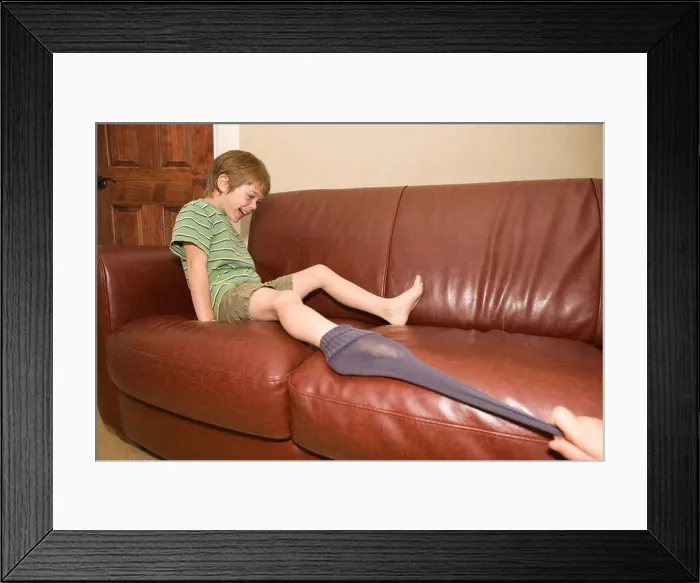 Framed Print : sibling pulling younger brother's sock off on sofa at home Framed Print : sibling pulling younger brother's sock off on sofa at home