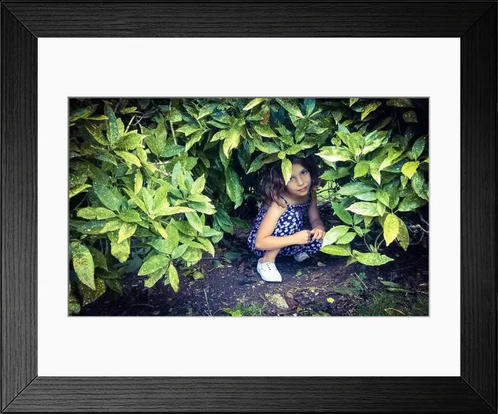 Framed Print : Young girl looking out from hiding place in bush Framed Print : Young girl looking out from hiding place in bush
