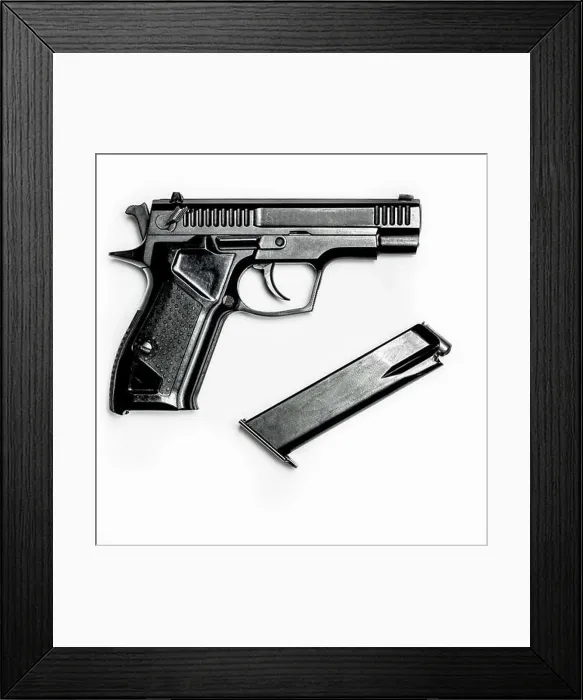 Framed Print : A black pistol with a magazine for cartridges lies on a white background Framed Print : A black pistol with a magazine for cartridges lies on a white background