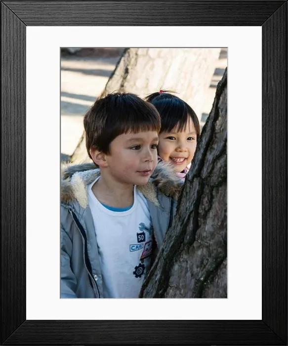 Framed Print : Children, Caucasian boy and Japanese girl, 4-5 year old. Girl smiling and behind the boy as she watches as he carves initials on tree trunk Framed Print : Children, Caucasian boy and Japanese girl, 4-5 year old. Girl smiling and behind the boy as she watches as he carves initials on tree trunk