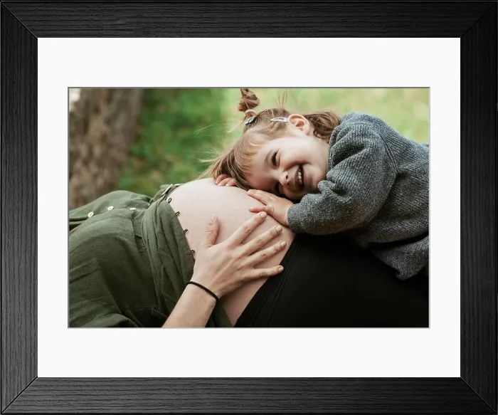 Framed Print : A sweet moment as a young girl with a big smile listens to a pregnant belly, bonding with the unborn sibling outdoors Framed Print : A sweet moment as a young girl with a big smile listens to a pregnant belly, bonding with the unborn sibling outdoors