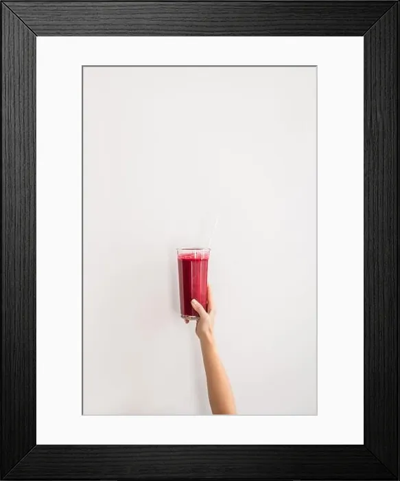 Framed Print : Human hand holding glass with purple beet pomegranate fresh smoothie with glass straw over white wall background, copy space