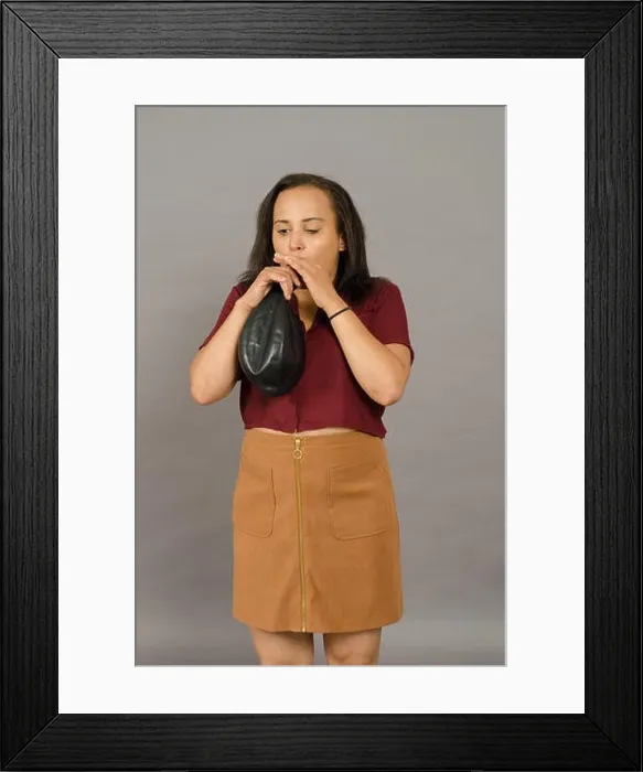 Framed Print : Adult woman blowing up a huge black balloon Framed Print : Adult woman blowing up a huge black balloon