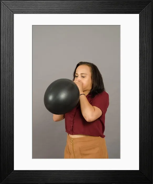 Framed Print : adult female blowing up a very large black balloon Framed Print : adult female blowing up a very large black balloon