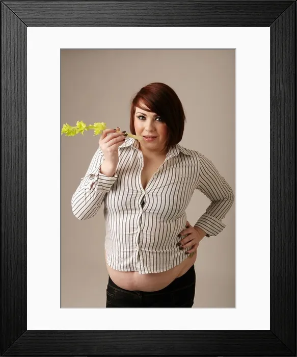 Framed Print : Overweight woman in a tight fitting shirt standing holding a stick of celery Framed Print : Overweight woman in a tight fitting shirt standing holding a stick of celery