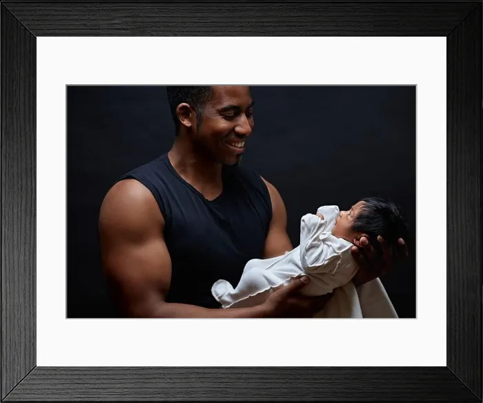 Framed Print : Young afro-american daddy holding his sweet newborn baby in the arms and looking at him with love. side view photo. first meeting with a adorable baby Framed Print : Young afro-american daddy holding his sweet newborn baby in the arms and looking at him with love. side view photo. first meeting with a adorable baby