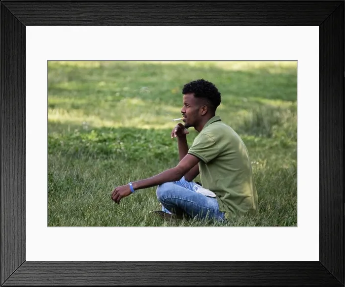 Framed Print : young man smokes sitting on the grass in the city park Framed Print : young man smokes sitting on the grass in the city park