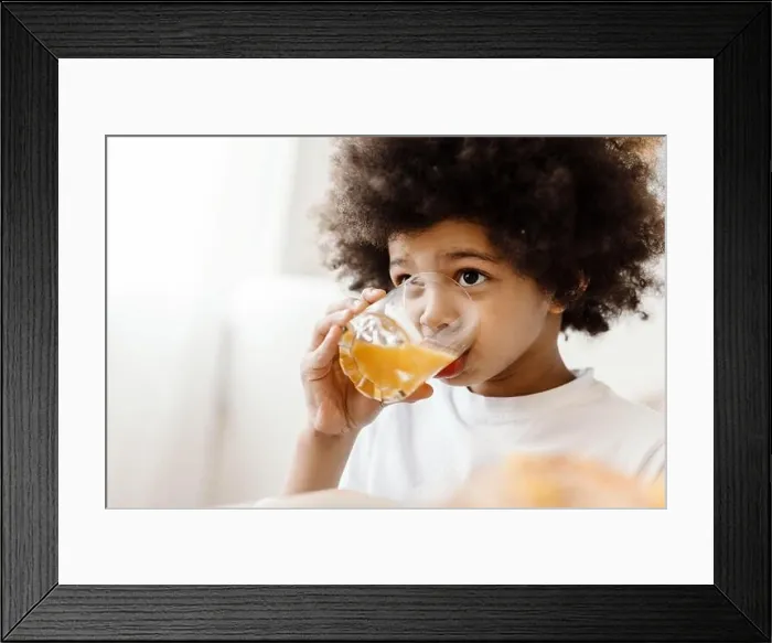 Framed Print : Black curly boy looking forward while drinking juice indoors Framed Print : Black curly boy looking forward while drinking juice indoors