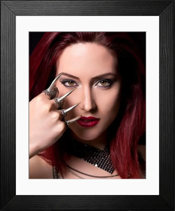 Framed Print : Red-haired woman with striking makeup wearing claw rings and looking at the camera against a black background Framed Print : Red-haired woman with striking makeup wearing claw rings and looking at the camera against a black background