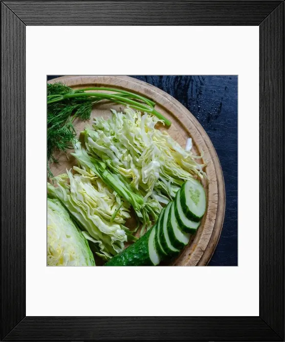 Framed Print : The process of making vegetable salad. Sliced fresh vegetables on a cutting board. Slaw white cabbage, cucumber and dill on a round cutting board. Sim Framed Print : The process of making vegetable salad. Sliced fresh vegetables on a cutting board. Slaw white cabbage, cucumber and dill on a round cutting board. Sim