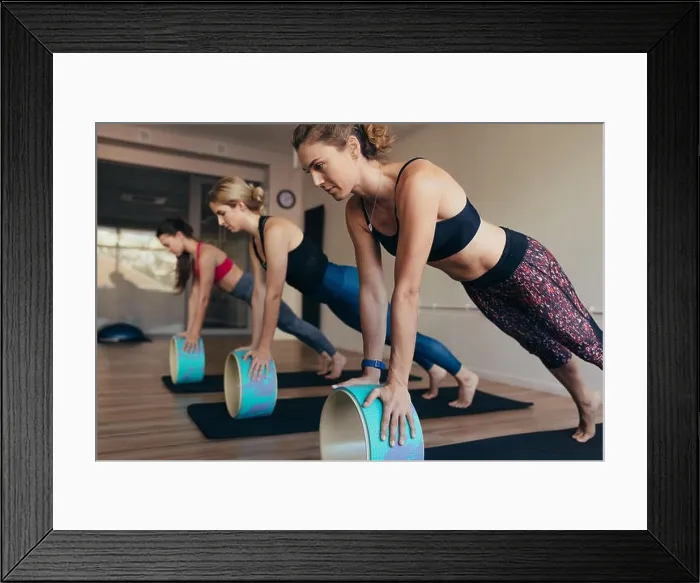 Framed Print : Women in push up position resting their hands on yoga wheel doing pilates workout. Three women doing pilates workout at the gym