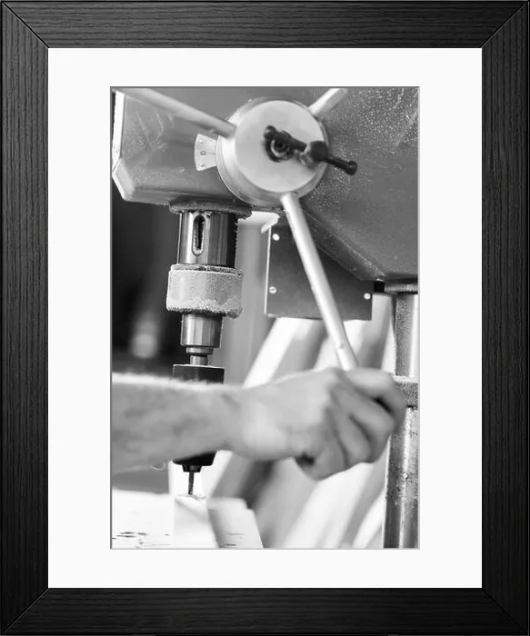 Framed Print : Close up view of a carpenter's hands operating a bench drill press on a piece of wood in a workshop. - black n white - Framed Print : Close up view of a carpenter's hands operating a bench drill press on a piece of wood in a workshop. - black n white -