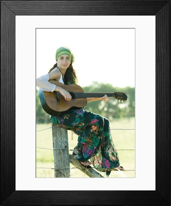 Framed Print : Young hippie woman sitting on fence post, playing guitar Framed Print : Young hippie woman sitting on fence post, playing guitar
