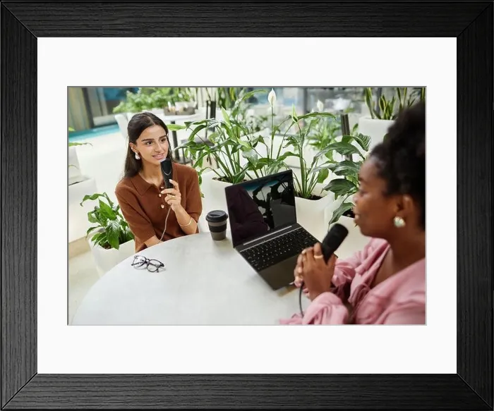 Framed Print : Medium shot of young businesswoman live streaming podcast with female guest sitting at cafe table equipped with laptop Framed Print : Medium shot of young businesswoman live streaming podcast with female guest sitting at cafe table equipped with laptop
