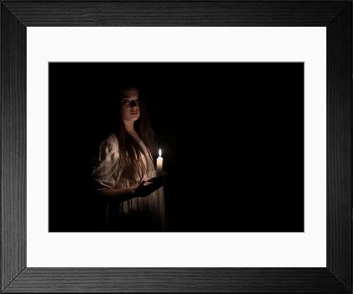 Framed Print : A young girl in an old white dress holding a candle in her hand and staring at the camera. Copy space on the right side. Dark background Framed Print : A young girl in an old white dress holding a candle in her hand and staring at the camera. Copy space on the right side. Dark background