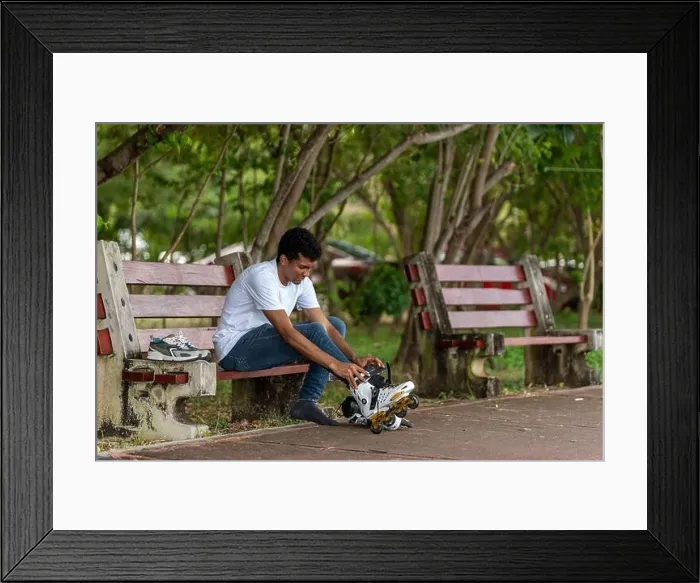 Framed Print : Young latino man sitting putting on inline skates Framed Print : Young latino man sitting putting on inline skates