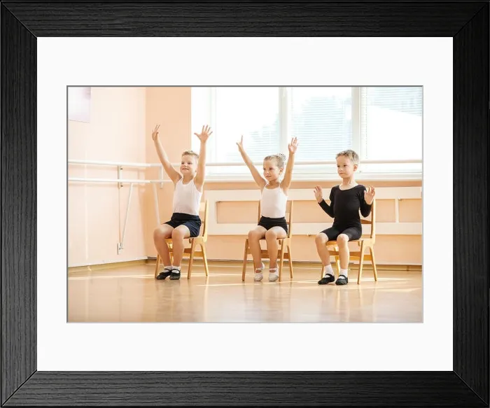 Framed Print : Young dancers playing or doing exercise while sitting on chairs at ballet class Framed Print : Young dancers playing or doing exercise while sitting on chairs at ballet class