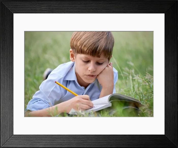Framed Print : Young people and education, school child doing homework, laying down on grass at park and studying with book. Medium shot Framed Print : Young people and education, school child doing homework, laying down on grass at park and studying with book. Medium shot