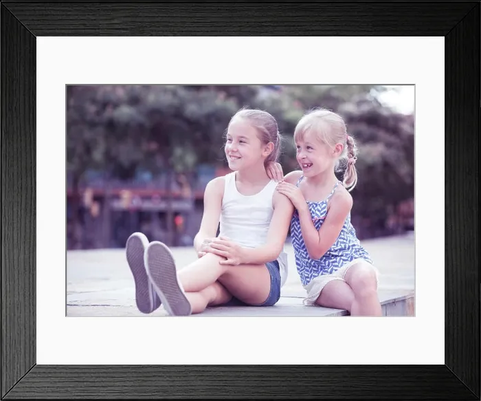 Framed Print : Two small happy sisters sitting outdoors, looking into distance Framed Print : Two small happy sisters sitting outdoors, looking into distance