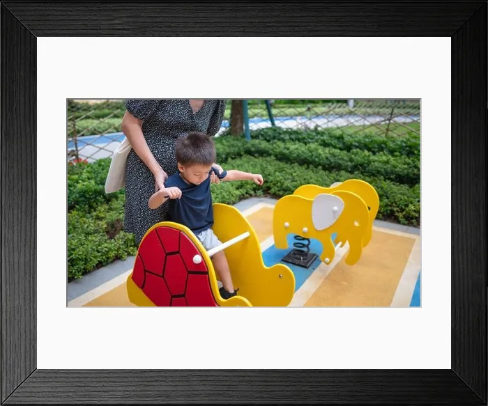 Framed Print : A cute two year old baby boy has fun playing on a colorful swing in the park, while his mom watches over his safety Framed Print : A cute two year old baby boy has fun playing on a colorful swing in the park, while his mom watches over his safety