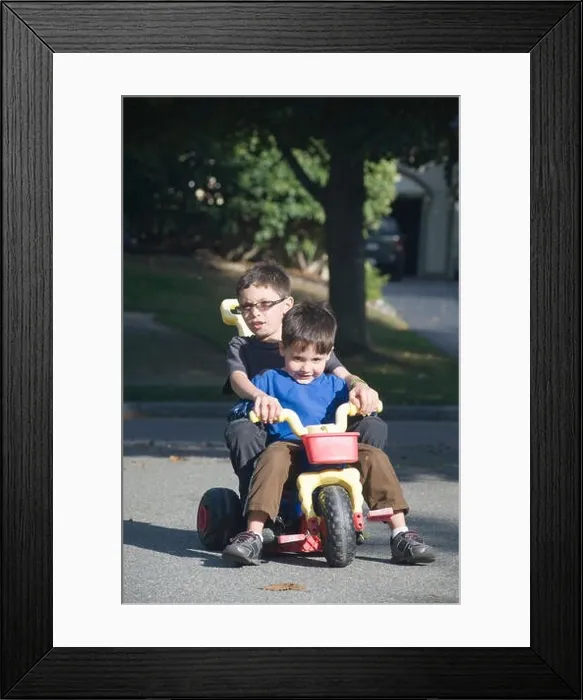Framed Print : Two brothers, age seven and four ride a big wheel three wheeler in their driveway Framed Print : Two brothers, age seven and four ride a big wheel three wheeler in their driveway
