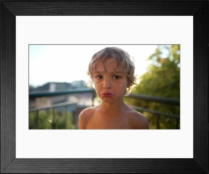Framed Print : Portrait of a young boy with sad expression. Sulky emotion of a little male kid standing outdoors looking at camera. Unhappy child Framed Print : Portrait of a young boy with sad expression. Sulky emotion of a little male kid standing outdoors looking at camera. Unhappy child