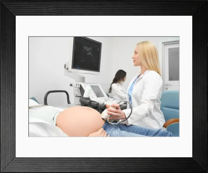 Framed Print : View from side of serious female doctor in white uniform doing ultrasound diagnostic to pregnant woman and looking at screen in clinic Framed Print : View from side of serious female doctor in white uniform doing ultrasound diagnostic to pregnant woman and looking at screen in clinic