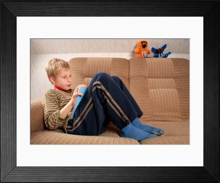 Framed Print : portrait of a young fair haired boy lying on a sofa and reading a book Framed Print : portrait of a young fair haired boy lying on a sofa and reading a book