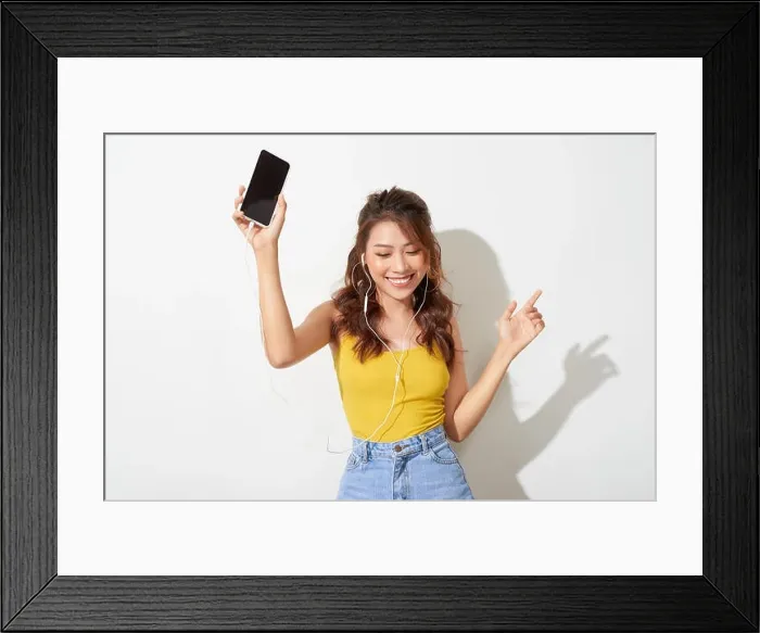 Framed Print : Portrait of a cheerful beautiful girl showing or presenting mobile phone application and pointing finger to sky Framed Print : Portrait of a cheerful beautiful girl showing or presenting mobile phone application and pointing finger to sky