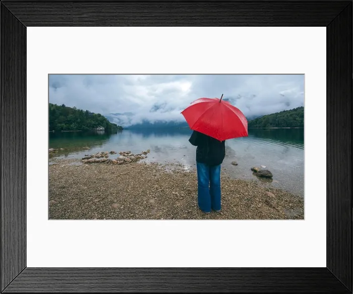 Framed Print : Woman with red umbrella contemplates on rain in front of a lake. Sad and lonely female person looking into distance Framed Print : Woman with red umbrella contemplates on rain in front of a lake. Sad and lonely female person looking into distance