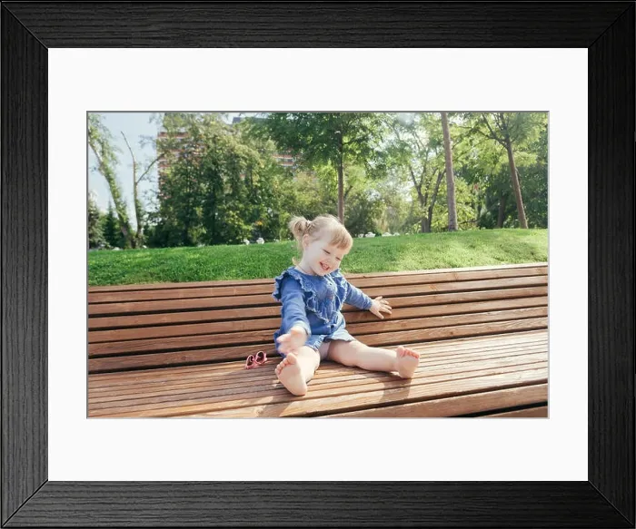 Framed Print : Little girl sitting on the bench and laughing in a city park on a warm sunny day Framed Print : Little girl sitting on the bench and laughing in a city park on a warm sunny day