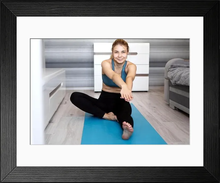 Framed Print : Sport, training and lifestyle concept - woman stretching leg on blue yoga mat at home in the living room
