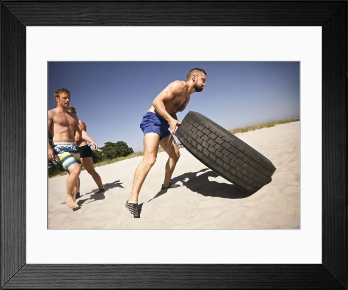 Framed Print : Tough male athlete flipping a truck tire. Young people doing crossfit exercise on beach Framed Print : Tough male athlete flipping a truck tire. Young people doing crossfit exercise on beach