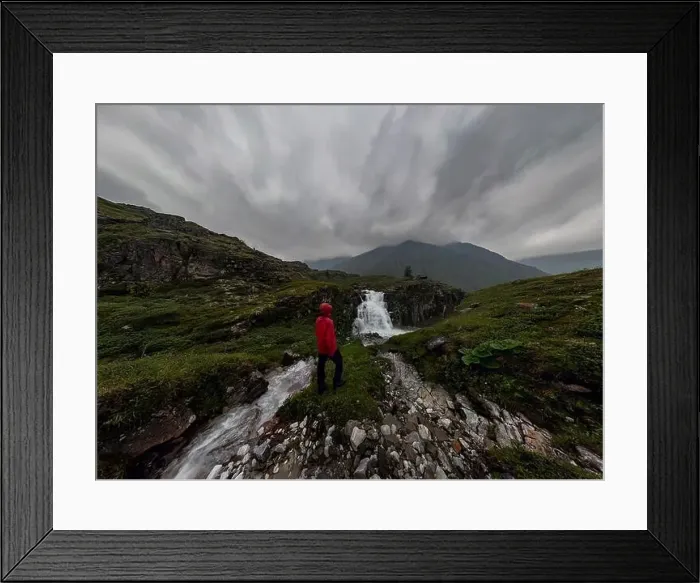 Framed Print : man in red stands under waterfall on black rock in mountains on cloudy rainy day.. Wide panorama Framed Print : man in red stands under waterfall on black rock in mountains on cloudy rainy day.. Wide panorama