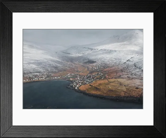 Framed Print : Aerial view of a Faroese village within a calm bay surrounded by snow-covered mountains as seen from a helicopter in Framed Print : Aerial view of a Faroese village within a calm bay surrounded by snow-covered mountains as seen from a helicopter in