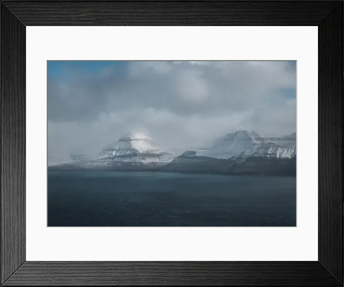 Framed Print : Aerial helicopter shot of snow-covered mountains at the shore of the Faroe Islands with low-hanging clouds during cold Framed Print : Aerial helicopter shot of snow-covered mountains at the shore of the Faroe Islands with low-hanging clouds during cold