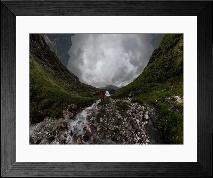 Framed Print : man in red stands under waterfall on black rock in mountains on cloudy rainy day.. Wide panorama